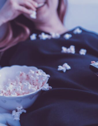 a woman eating popcorn on a sofa holding a tv remote