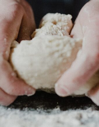 two hands kneading dough on a floury surface