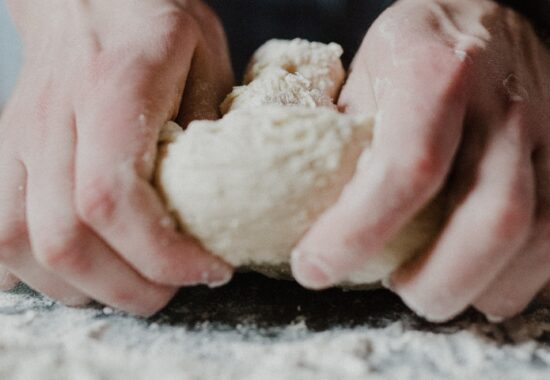 two hands kneading dough on a floury surface