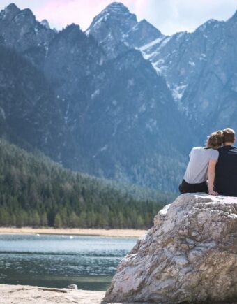 a couple sits on a rock looking out over a lake